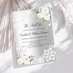 an elegant wedding card with white flowers and lace on the front, next to a fan