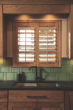 a kitchen window with wooden shutters and green tile backsplash above the sink