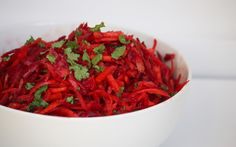 a white bowl filled with red food and garnished with cilantro leaves