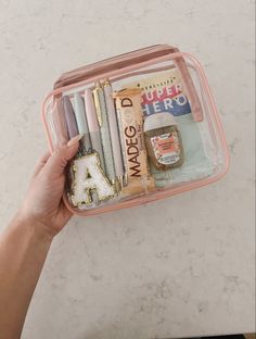 a person holding a pink case filled with writing and pencils on top of a table