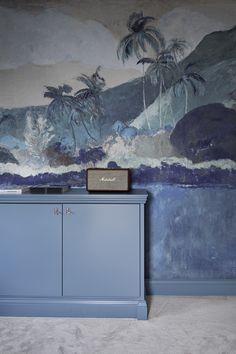 a blue cabinet sitting in front of a wall with palm trees painted on the walls