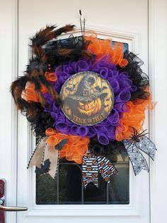 a halloween wreath on the front door decorated with orange and purple mesh, black feathers and a skeleton