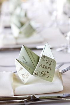 two folded origami pieces sitting on top of a napkin next to silverware