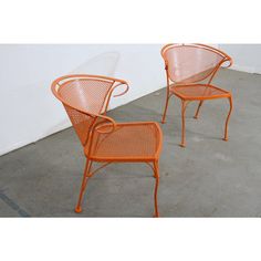 two orange metal chairs sitting next to each other on cement floored area with white wall in background