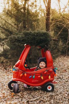 a small child in a red car with christmas lights on it's roof and trees growing out of the top