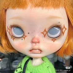 a close up of a doll with orange hair and blue eyes wearing a green sweater