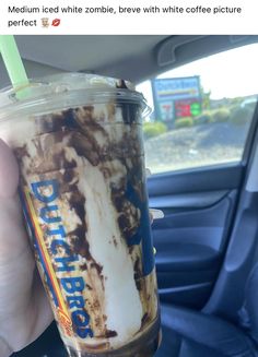 a person holding up a cup with ice cream and coffee in it on the back seat of a car