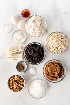 an assortment of ingredients in bowls on a white counter top, including eggs, flour and chocolate