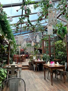 the inside of a greenhouse filled with lots of plants and hanging chandeliers over tables