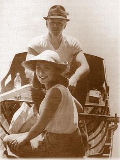 an old photo of two people sitting on a boat together, one is holding a paddle and the other is wearing a hat