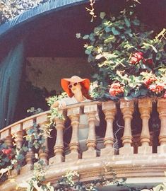 a woman wearing a red hat and sunglasses sitting on a balcony with flowers in the background