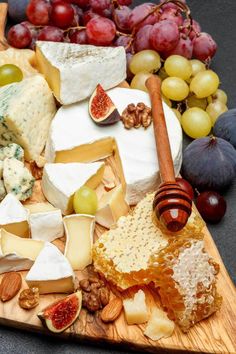 a wooden cutting board topped with different types of cheese and fruit on top of it