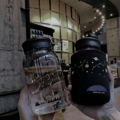 two people holding up mason jars in front of a building with stars and planets on them