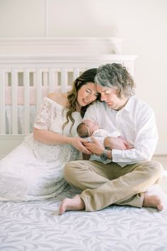 a man and woman sitting on top of a bed holding a baby