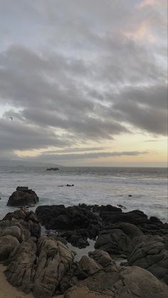 a person standing on top of a rock covered beach next to the ocean under a cloudy sky