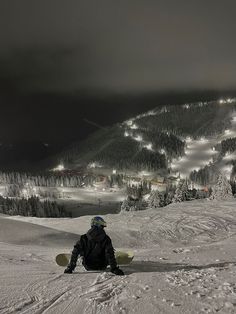 a man sitting on top of a snow covered slope next to a ski slope at night