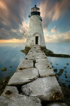 a light house sitting on top of a stone pier next to the ocean under a cloudy sky