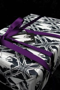 two wrapped presents with purple ribbon on black and white wrapping paper, one is folded in the shape of a cross