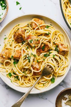 a plate of pasta with meatballs and parsley on the side next to two bowls