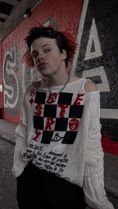 a woman with red hair standing in front of a graffiti wall wearing a white shirt and black skirt