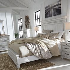 a white bed sitting in a bedroom on top of a wooden floor next to two windows