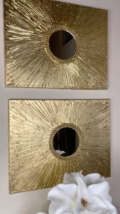 two gold wall mirrors with white flowers in the foreground and one on the right