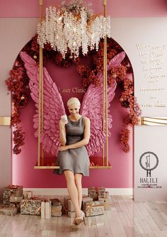 a woman sitting on a swing in front of a pink wall with an angel decoration