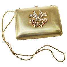 Saks Fifth Avenue Italian gilt metal crystal medallion minaudiere' evening bag c 1980s The elegant gold metal evening bag has a satin matte finish. The front exterior panel is adorned with a sinuous medallion encrusted with diamante & jewel crystals The versatile evening bag can be carried as a chic clutch; transitions into a stylish shoulder bag carried with the snake style chain strap. The interior is lined in black felt labeled Saks Fifth Avenue Made in Italy The clasp mechanism is placed on the top center section with a wreath of crystals Pressing down on the circular center black glass stone releases the evening bag open The length measures 5.75 inches The height measures 4 inches The drop length from the top of the shoulder strap to the bag base = 24 inches Stylish Shoulder Bag, Black Felt, Black Glass, Fashion Handbags, Chain Strap, Saks Fifth, Saks Fifth Avenue, Evening Bags, Metallica