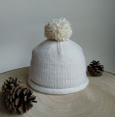 a white knitted hat sitting on top of a wooden table next to pine cones