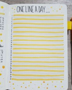 an open planner with yellow and white stripes on it, next to a pen that says one line a day