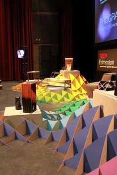 the stage is set up for an event with colorful paper structures on it and a projector screen in the background