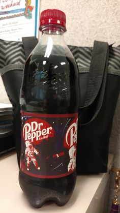 a bottle of dr pepper soda sitting on top of a counter next to a purse