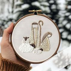 a person holding up a small embroidery hoop with two sheep and umbrellas on it