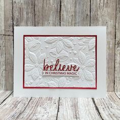 a christmas card with the words believe in red and white, on a wooden background