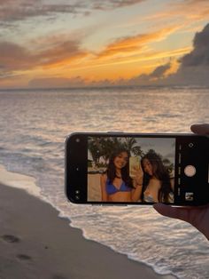 a person holding up a cell phone to take a photo on the beach at sunset