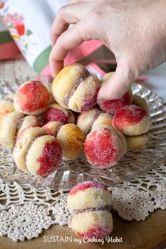 a person is picking up some sugary pastries from a glass plate on a doily