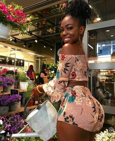 a woman standing in front of flowers holding a watering can