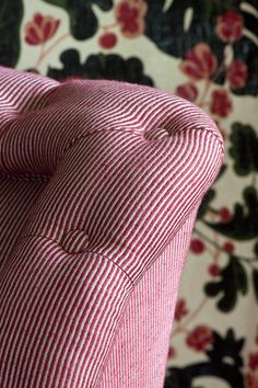 a red and white striped pillow on a floral wallpapered chair with buttons at the back