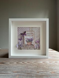 a white frame with purple flowers and butterflies in it on top of a wooden table