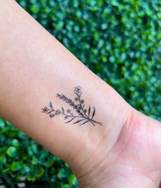 a small tattoo on the wrist of a woman's arm with flowers and leaves