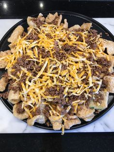 a black plate topped with cheesy meat and cheese covered nachos on top of a marble counter