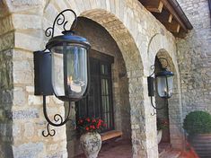 an old fashioned light hanging from the side of a stone building with potted flowers