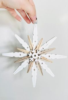 a hand holding a wooden snowflake ornament in front of a white wall