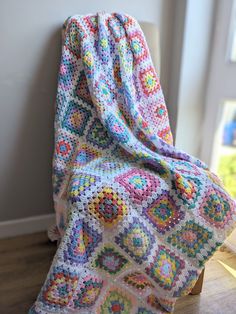 a colorful crocheted blanket sitting on top of a wooden floor next to a window