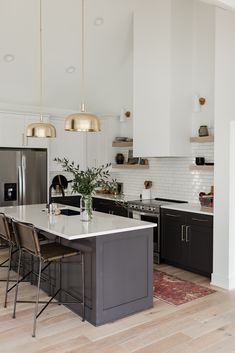 a kitchen with black and white cabinets, an island countertop and gold pendant lights