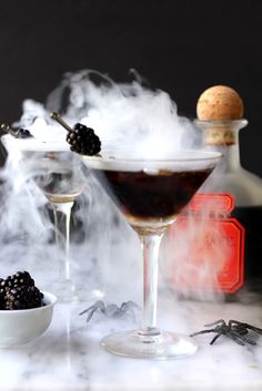 two glasses filled with liquid and blackberries next to a bottle of booze on a table