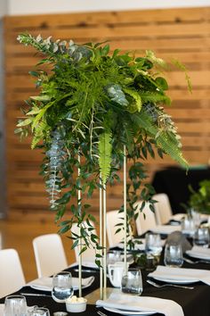 there is a tall plant in the center of this table with white plates and silverware