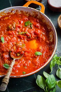 a large pot filled with lots of red sauce and green leaves on top of it