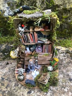 a miniature book shelf filled with books on top of a stone wall covered in moss