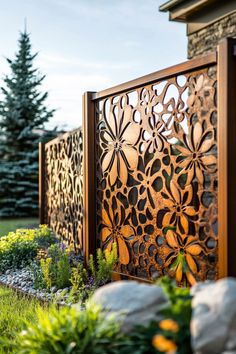 a wooden fence with flowers on it in front of some rocks and grass near a house